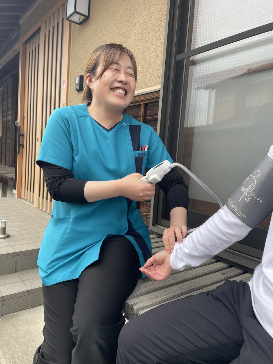 屋外で笑顔でご利用者さまの血圧を測るいろはのスタッフ